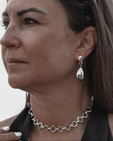 Woman wearing silver jewelry including a necklace, earrings, and rings against a neutral background.