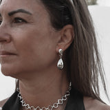 Woman wearing silver jewelry including a necklace, earrings, and rings against a neutral background.