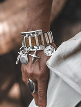 Chunky cuff bracelet in silver with brown snake leather, featuring dangling silver charms, worn on a wrist.