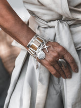 Chunky silver cuff bracelet showcasing brown snake-print leather and multiple dangling charms, worn on a wrist.