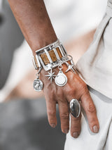Chunky silver cuff bracelet featuring brown snake leather and dangling silver charms, worn on a model's wrist.