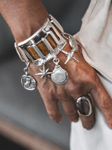 Chunky silver cuff bracelet featuring brown snake-print leather, adorned with five silver charms, showcased on a wrist.
