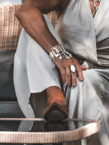 Brown snake leather and silver chunky cuff bracelet with dangling charms, worn on a wrist, paired with a light outfit.