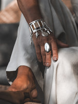 Chunky silver cuff bracelet featuring brown snake leather and five dangling charms, worn on a model's wrist.