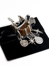 Chunky cuff bracelet featuring brown snake-print leather and five dangling silver-plated charms, set on a black suede pouch.