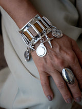 Chunky silver cuff bracelet featuring brown snake leather and dangling silver charms, worn on a model's wrist.