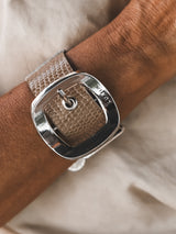 Textured beige leather cuff bracelet with a prominent silver buckle, worn on a wrist against a neutral background.