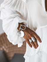 Chunky silver-plated shackle bracelet with large coin pendants and industrial clasp, worn on a wrist with two silver rings.