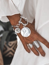 Silver-plated shackle bracelet with large coin pendants, chunky design, worn on a model's wrist with a ring.