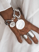 Chunky silver-plated shackle bracelet featuring large ancient coin pendants, worn on a hand with silver rings.