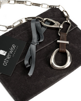Edgy choker necklace featuring a large silver buckle and hammered iron chain, set against a dark suede pouch.