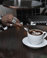Adjustable silver spiral design ring worn on a hand stirring coffee, paired with multiple shiny bangles.