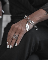Adjustable silver spiral design ring worn on a hand with trendy white nails, paired with a chunky silver bracelet.