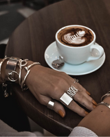 Boho silver spiral statement ring worn alongside various silver bangles, displayed with coffee on a wooden table.