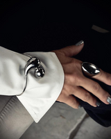 Elegant stainless steel cuff bracelet with large drops, worn over a white shirt sleeve on a wrist, showcasing an edgy style.