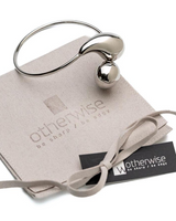Adjustable stainless steel cuff bracelet with large drops, styled over an elegant suede pouch with a bow and branding tag.