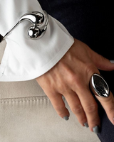 Elegant stainless steel cuff bracelet worn over a white sleeve, featuring large rounded drops. Hand shows a chunky silver ring.