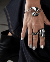 Adjustable stainless steel cuff bracelet with large drops worn on the wrist, paired with chunky rings and silver nail polish.