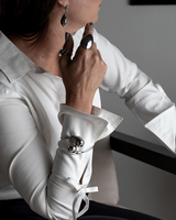 Elegant stainless steel cuff bracelet worn over a white long-sleeve shirt, featuring large drop details.