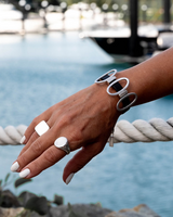 Black leather cuff bracelet featuring oval metal elements, worn on a model's wrist against a scenic backdrop.