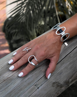 Black leather cuff bracelet featuring oval metal elements, worn on a hand with white nails, paired with silver rings.