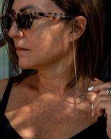 Thin silver box chain necklace worn as a glasses holder with black silicone loops, paired with a black spaghetti strap top.