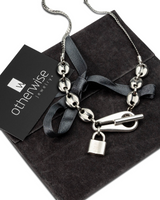 Stainless steel choker necklace featuring a padlock pendant and chunky anchor link chain, resting on a suede pouch.
