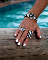Adjustable bracelet featuring a large grey-black triangular Austrian crystal, paired with similar rings on a model’s hand.