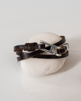Brown leather wrap bracelet features three strands and a silver zamak buckle, displayed on a white stone.