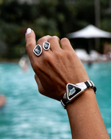 Grey-black triangular Austrian crystal bracelet in Zamak metal, worn on a hand with matching rings, set against a pool backdrop.