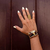 Gold plated adjustable ring with a chunky design, worn on a model's hand against a dark wood background.