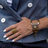 Gold plated chunky ring with a ridged design, worn on a hand with white nails, paired with a stylish wrist bracelet.
