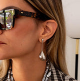 Large, abstract silver earrings with a chunky water drop shape, worn by a model with sunglasses.