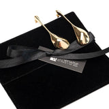 Large long abstract earrings in gold, featuring a sculptural water drop design, displayed on a black suede pouch.