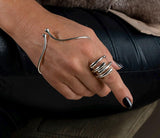 Irregular wrap unisex ring in shiny silver worn stacked with two other silver rings on a hand with black nail polish.