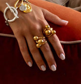 Chunky gold and silver triple ball rings, featuring large spheres, worn on a model's hand with a neutral manicure.