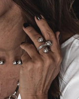 Adjustable stainless steel ring featuring three large spheres, worn on the index finger, paired with a chunky necklace.