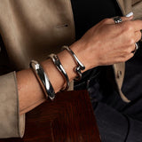 Chunky silver cuff bangles worn stacked on a wrist, showcasing a sleek, polished design with varying thicknesses.