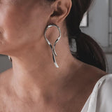 Large silver asymmetric dangle earrings with irregular, twisted lines, creating a bold statement look.