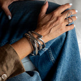 Chunky silver cuff bangles stacked on a wrist, featuring a sleek, polished design, paired with a slim silver ring.