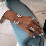 Silver plated open bangle cuff worn on a wrist, featuring a sleek and modern design, paired with a chunky silver ring.