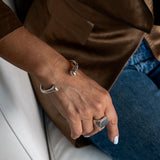 Unisex silver plated open bangle bracelet worn on a hand, featuring smooth curves and a polished finish.