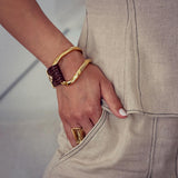 Chunky gold-plated metal and brown leather bracelet worn on a model's wrist, styled with a textured finish.