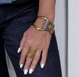 Chunky gold-plated bracelet featuring olive green leather, worn on a wrist with a statement ring; casual yet edgy style.