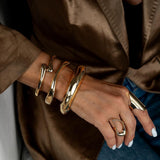 Chunky gold metal cuff bangles stacked on a wrist, featuring varying thicknesses, worn with a stylish ring.