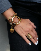 Gold triple wrap bracelet with beige leather features a large metal hoop and stainless steel chain, worn on a wrist.