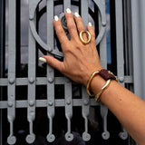 Unisex leather and gold plated chunky bracelet featuring a brown leather band and unique metal design, worn on a hand.