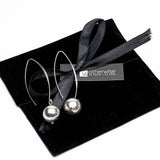 Chunky silver drop earrings with elongated hooks and shining spheres, presented on a black suede pouch with a ribbon.