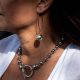 Chunky silver metal ball drop earrings hang from elongated hooks, paired with a matching beaded necklace on a model.