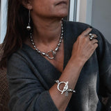 Chunky silver ball drop earrings hanging from eco hooks, worn by a model with layered silver jewelry and a gray sweater.